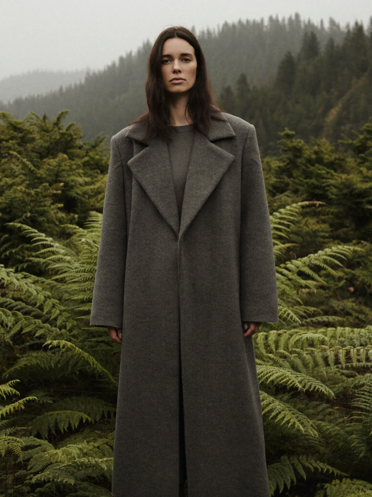 Woman wearing a charcoal grey long wool blend overcoat among sword ferns