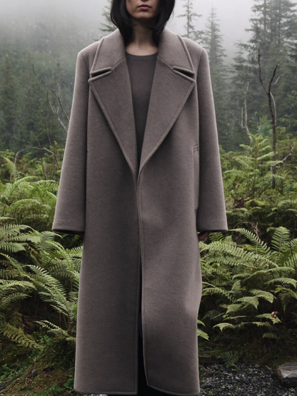 Woman wearing a warm taupe long wool blend overcoat among sword ferns