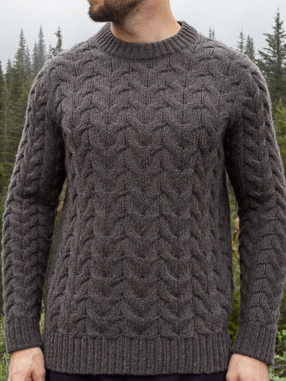 Man wearing a charcoal grey chunky cable knit wool sweater in a misty forest