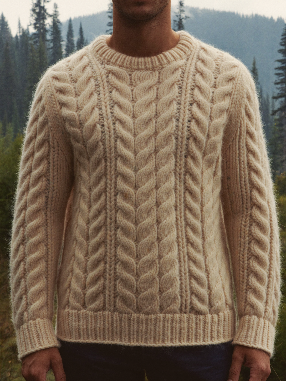 Man wearing an oatmeal chunky cable knit wool sweater in a misty forest