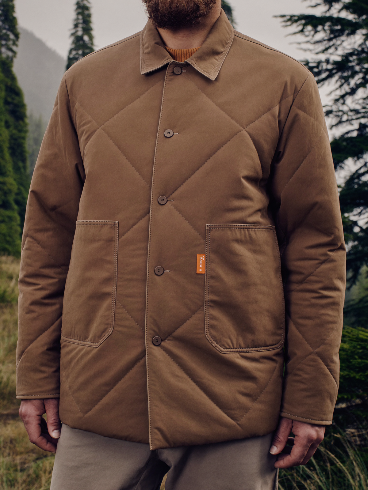 Person wearing a bark brown insulated quilted shirt jacket in a misty forest
