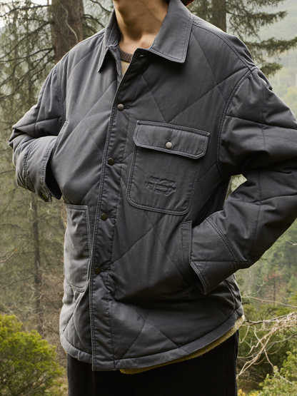 Person wearing a charcoal grey insulated quilted shirt jacket in a misty forest