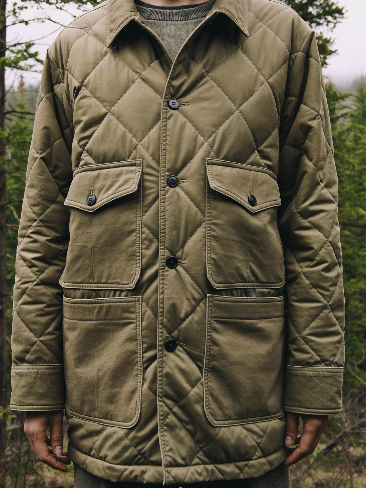 Person wearing a muted olive insulated quilted shirt jacket in a misty forest