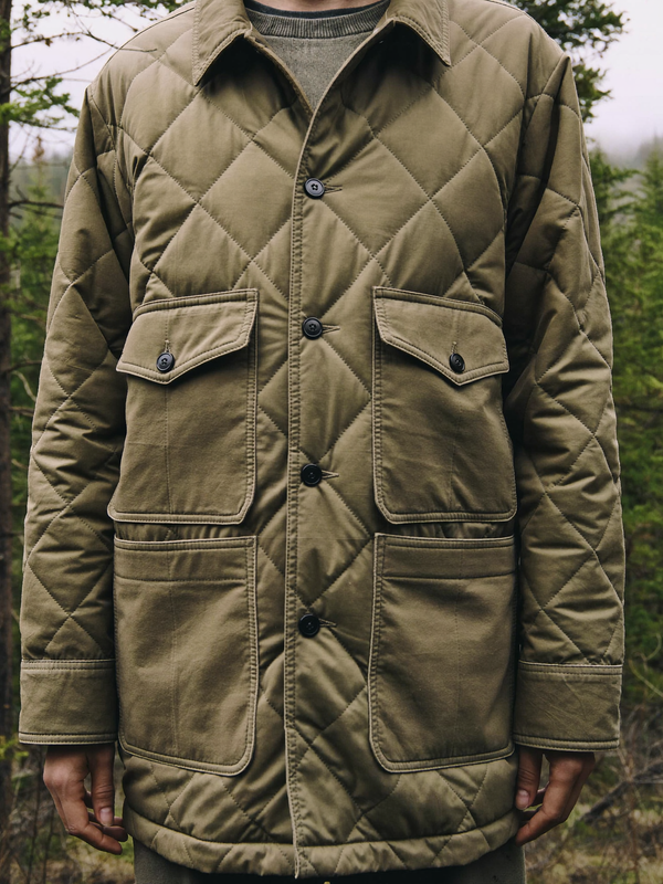Person wearing a muted olive insulated quilted shirt jacket in a misty forest